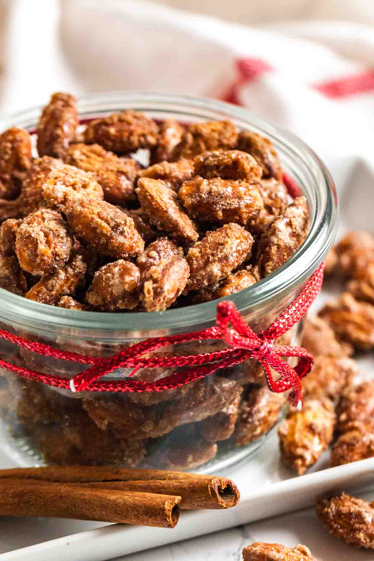 A glass bowl of cinnamon candied almonds with a red ribbon around it next to some more of the almonds.
