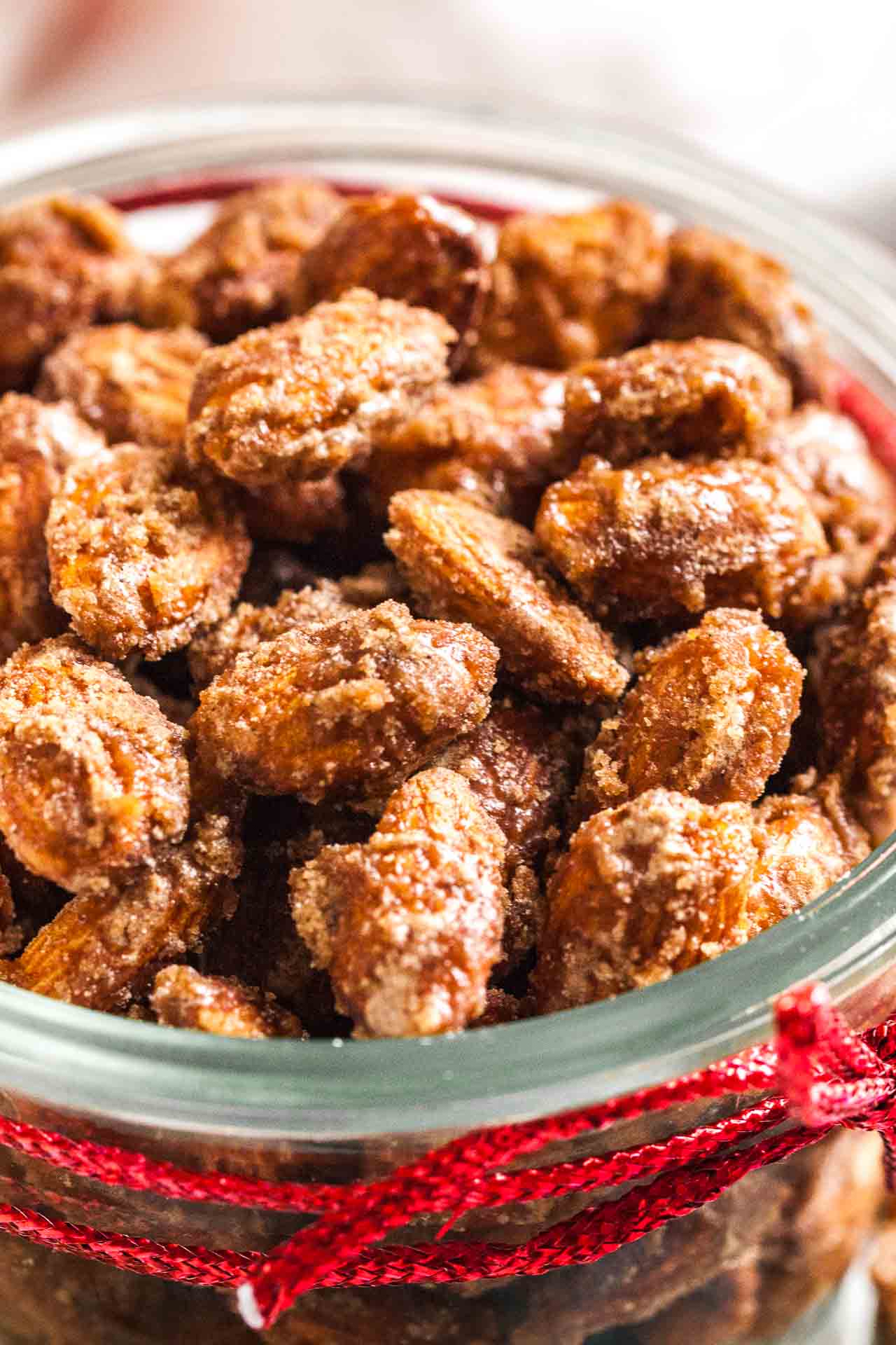 A glass bowl of cinnamon candied almonds with a red ribbon around it.