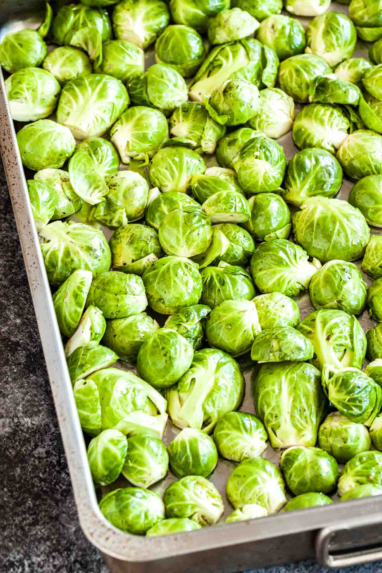 Halved, raw brussels sprouts, covered in oil, salt and pepper on a baking sheet.