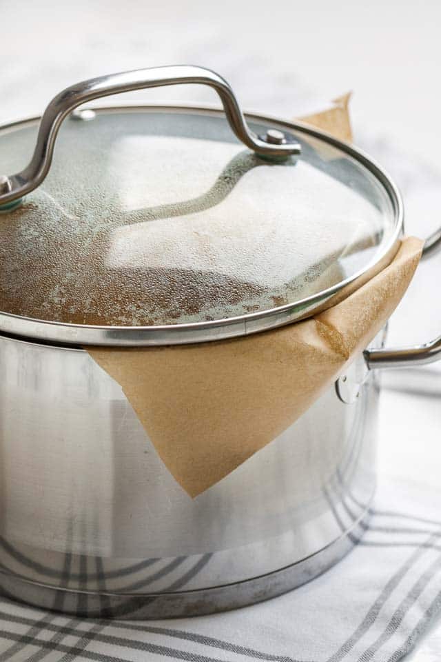 A stainless steel pot, lined with parchment paper, with a fogged-up glass lid.