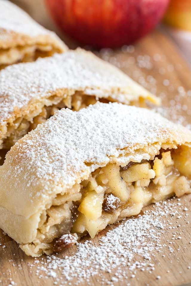 Close-up of several pieces of apple strudel topped with powdered sugar on a wooden cutting board.