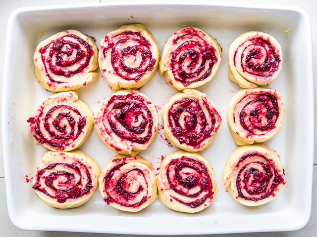 Top-down shot of a white baking dish with unbaked cranberry-orange rolls in them.