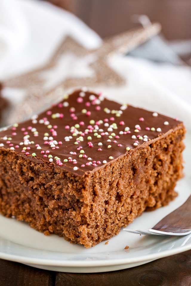 Close-up of a white plate with a square of chocolate topped spice cake with a fork.