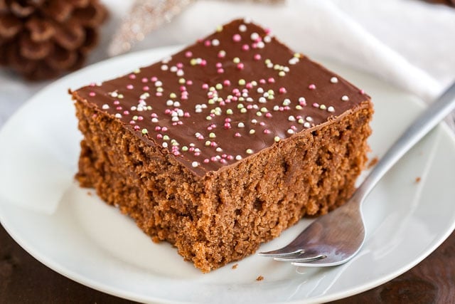 A white plate with a square of chocolate topped spice cake with a fork.