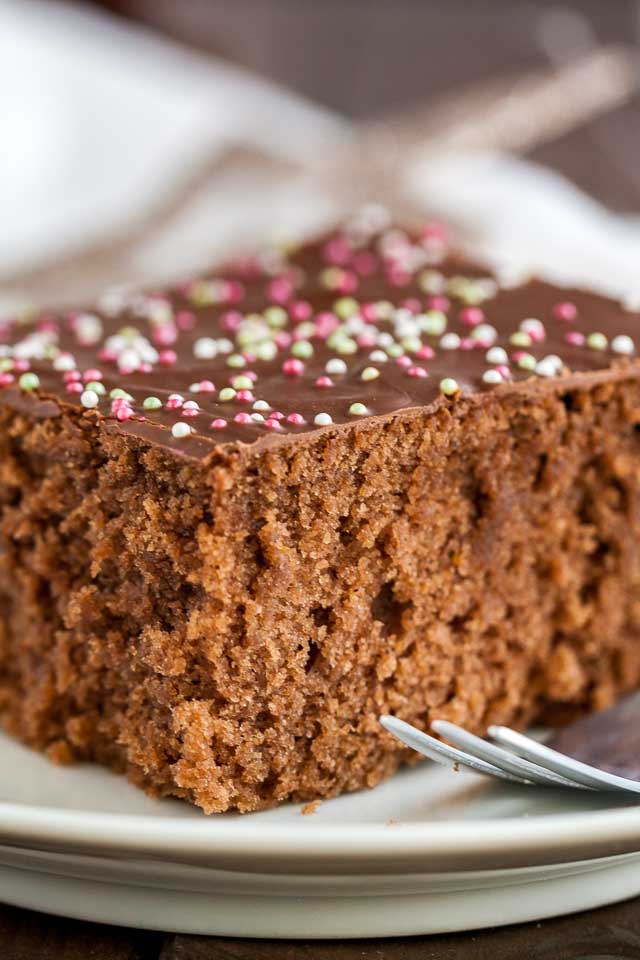Close-up of a piece of chocolate topped spice cake with a fork on a white plate.