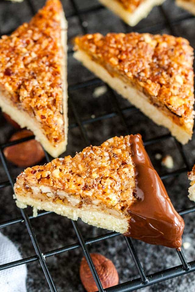 Close-up of nut corners with one chocolate-dipped corner on a black cooling rack over a dark surface.