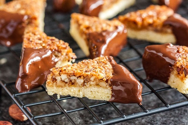 Nut corners with one chocolate-dipped corner on a black cooling rack over a dark surface.