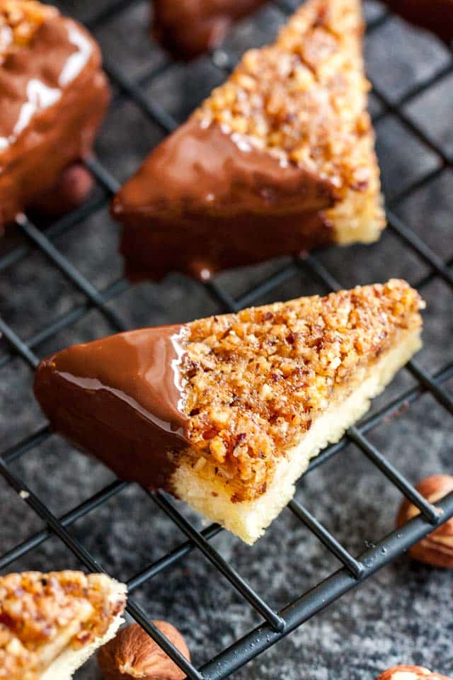 Close-up of nut corners with one chocolate-dipped corner on a black cooling rack over a dark surface.