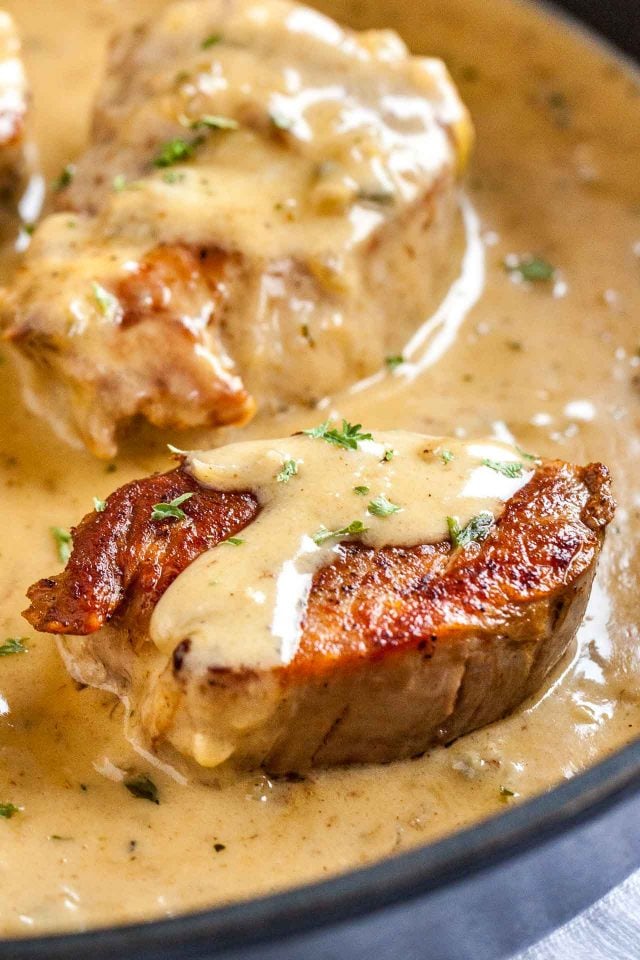 Two pan-pan seared pork medallions in a pan with blue cheese sauce, partially covered in blue cheese sauce.