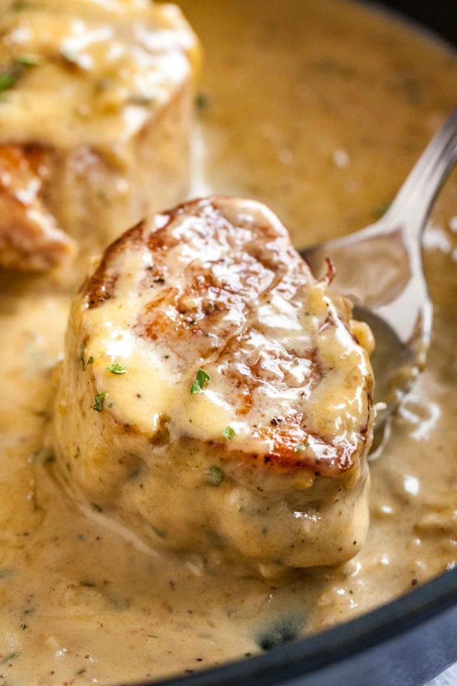 Close-up of a  seared pork medallion with blue cheese sauce on a spoon.