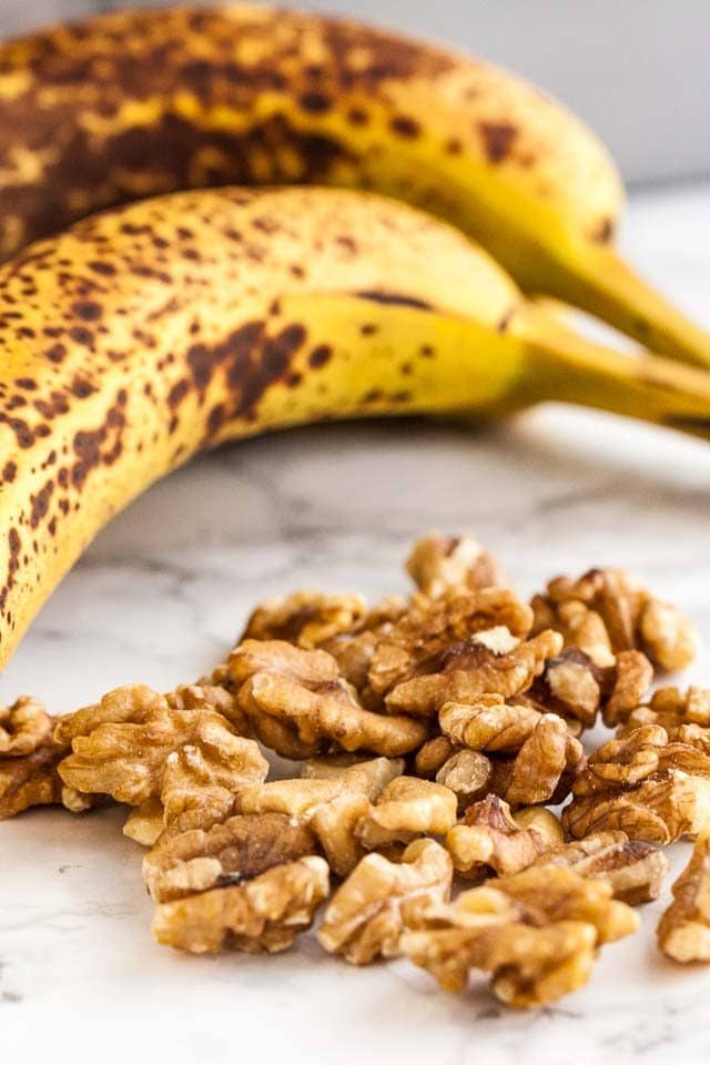Some walnuts in front of ripe bananas on a marble surface.