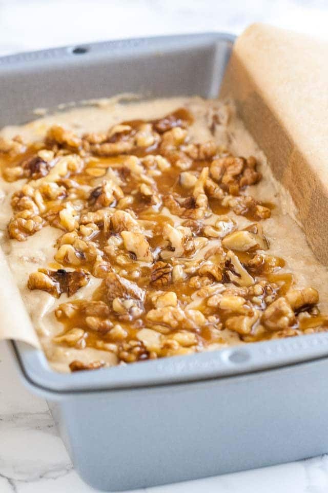 A bread pan, lined with parchment paper, filled with banana nut bread batter, topped with walnuts and caramel.