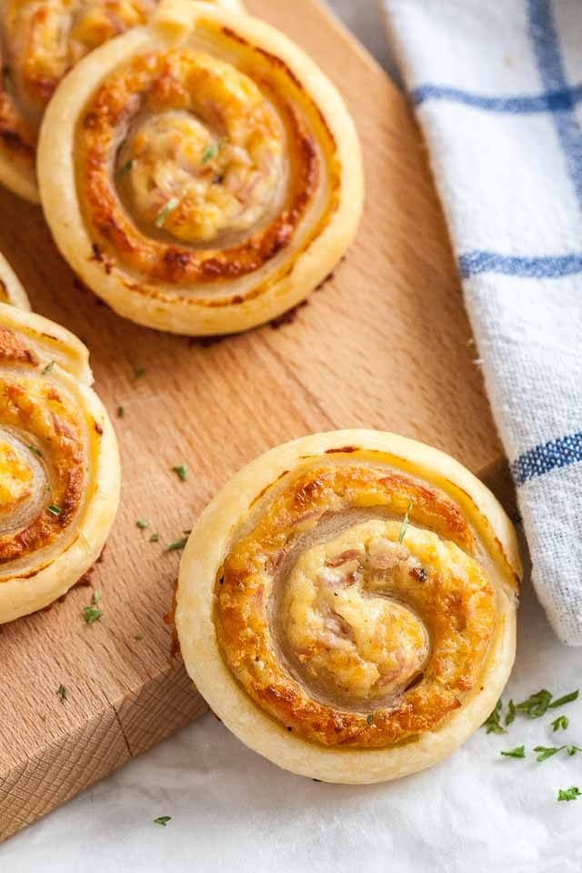 Top-down shot of ham and cheese pinwheels on a wooden cutting board with a white and blue dishtowel.
