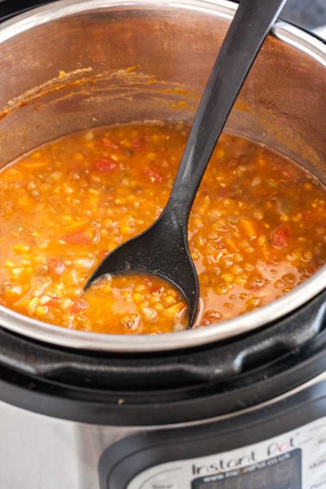 An instant pot with lentil soup with a black cooking spoon in it.