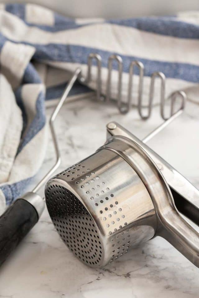 A potato ricer and a potato masher with a white and blue dishtowel.