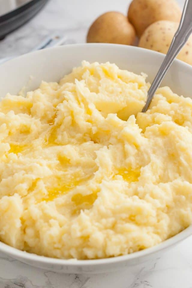 Close-up of a white bowl with mashed potatoes and a spoon.