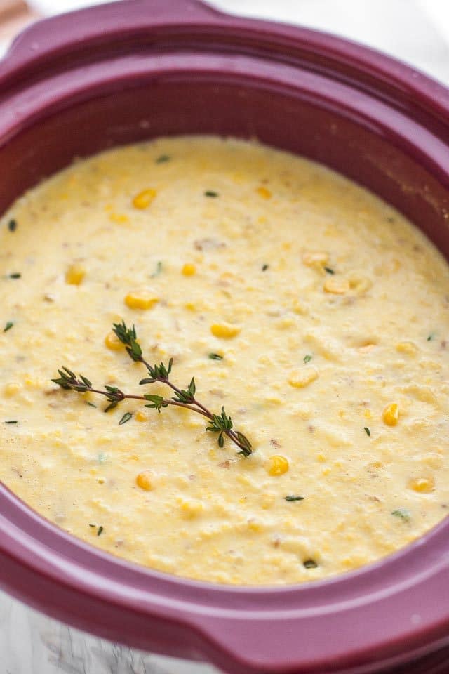 A red slow cooker pot with corn chowder with a sprig of thyme on top.