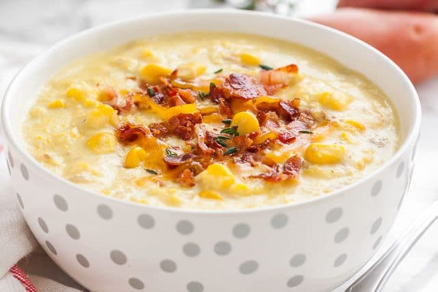 Close-up of a white bowl with silver dots of corn chowder topped with bacon bits and thyme.