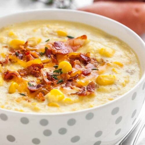 A white bowl with silver dots of corn chowder topped with bacon bits and thyme.