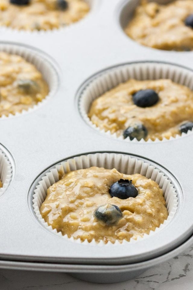 A muffin pan lined with paper baking cups filled with batter and blueberries.