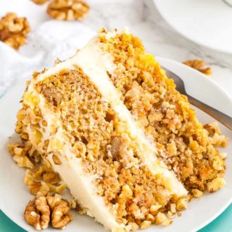 A slice of carrot pineapple cake garnished with walnuts lying on its side on a white plate stacked on a teal plate with a fork.