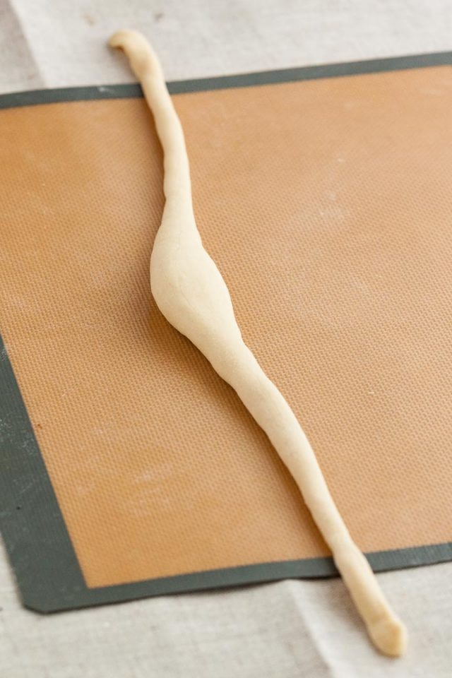 Pretzel dough rolled into a long sausage shape with a thick middle part on a silicon baking mat.