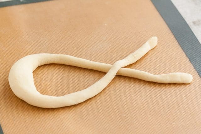 Pretzel dough, after being shaped into a sausage shape, laid out into a ribbon shape on a silicon baking mat.