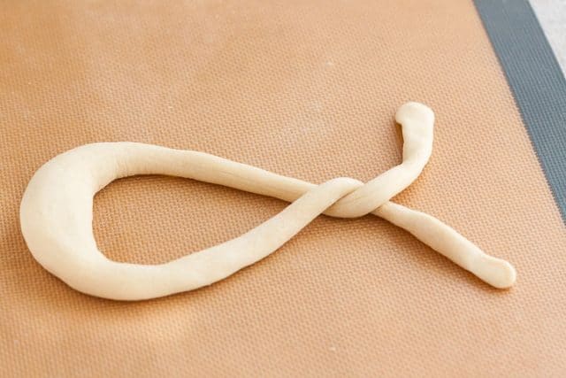 Pretzel dough laid out into a ribbon and twisted around the point of contact once on a silicon baking mat.