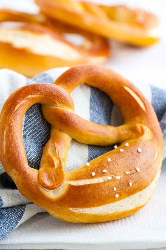 Close-up of a pretzel leaning against a folded white and blue towel, with more pretzels in the background.