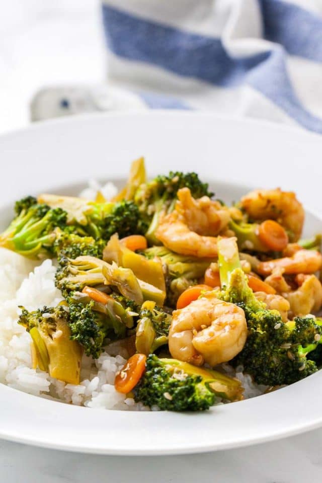 A plate of rice topped with shrimp and broccoli stir fry next to a white and blue dishtowel.