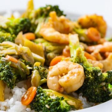 A plate of rice topped with shrimp and broccoli stir fry.