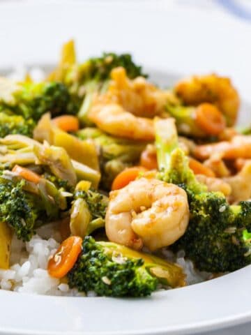 A plate of rice topped with shrimp and broccoli stir fry.
