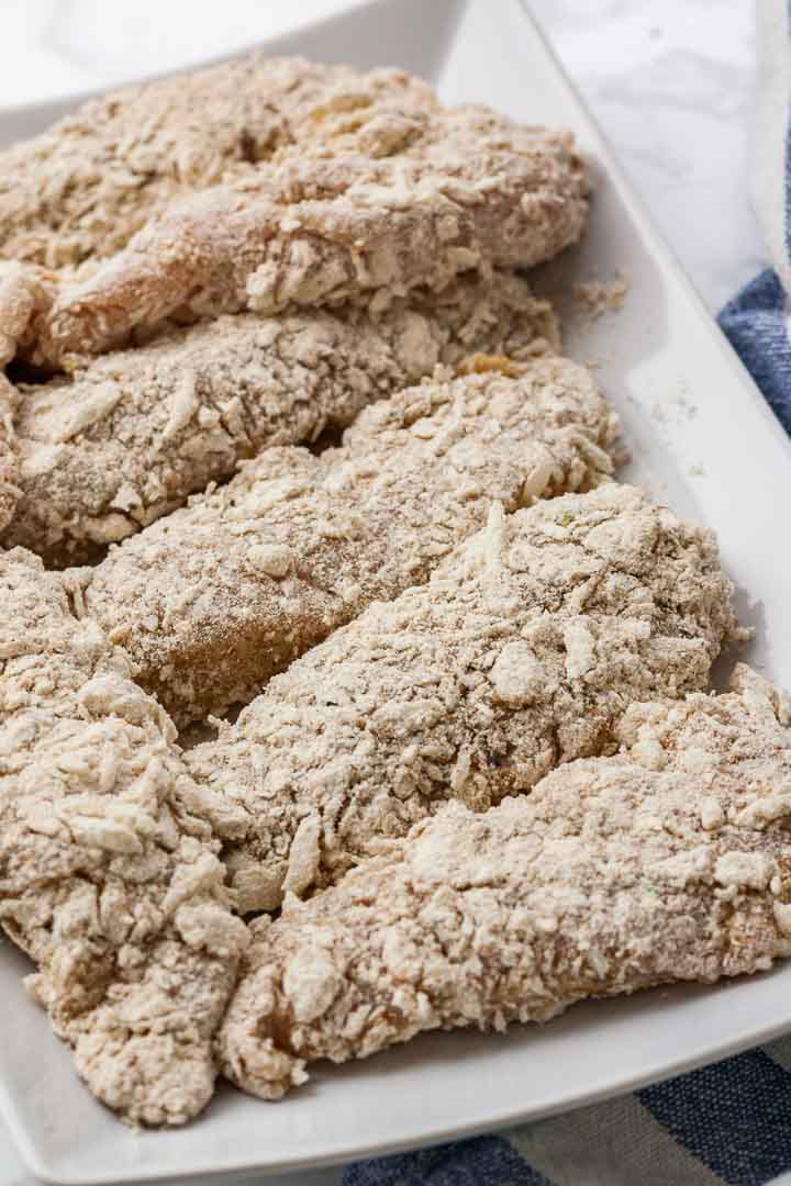 Breaded chicken tenders lying next to each other on a white serving platter.