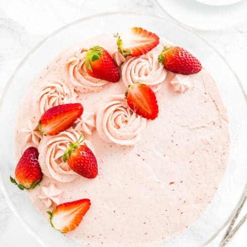 Top-down shot of a strawberry cake topped with strawberries on a glass serving dish.