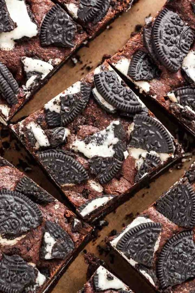 Top-down shot of oreo brownies topped with oreo cookies, freshly cut into squares on parchment paper.
