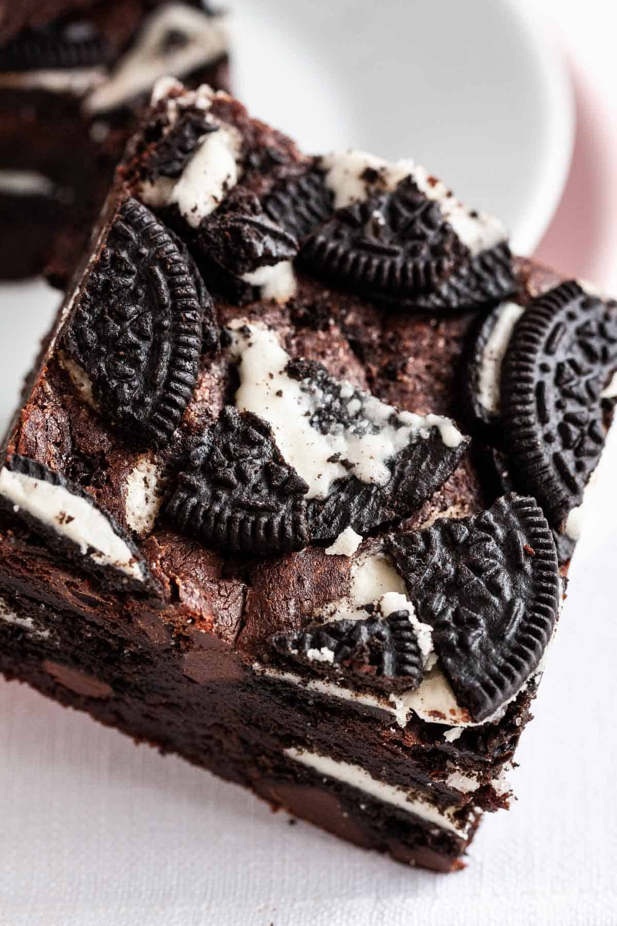 A brownie with Oreo cookies on top leaning against a plate.