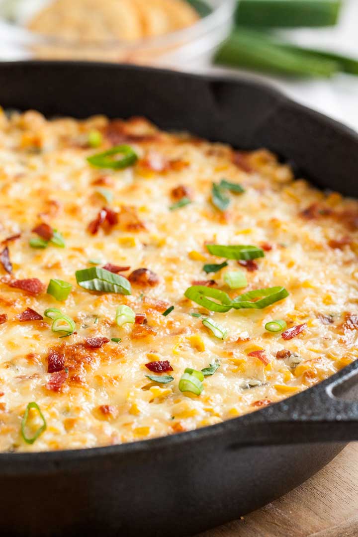 A lodge pan with hot corn dip topped with molten cheddar and spring onions.