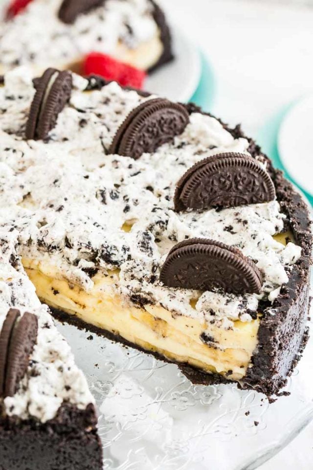Oreo banana cream cake with a slice missing on a glass serving dish.
