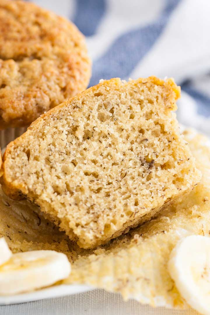 Close-up of an unwrapped and halved muffin with a muffin and a blue and white dish towel in the background.