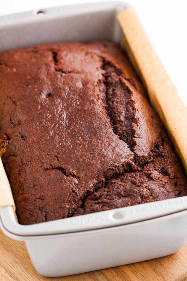 A bread pan, lined with parchment paper, containing a chocolate banana bread.