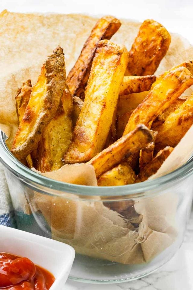 A Weck jar, lined with parchment paper, with brown, crispy fries standing in them.