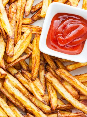 Top-down shot of brown, crispy fries with a small, white, rectangular bowl of ketchup.
