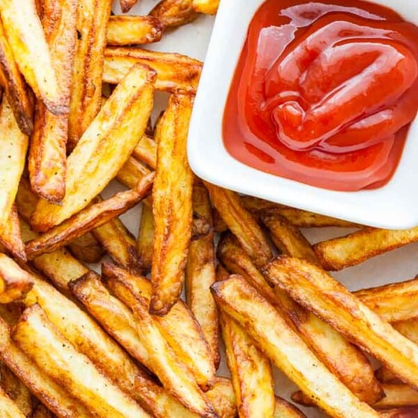 Top-down shot of brown, crispy fries with a small, white, rectangular bowl of ketchup.