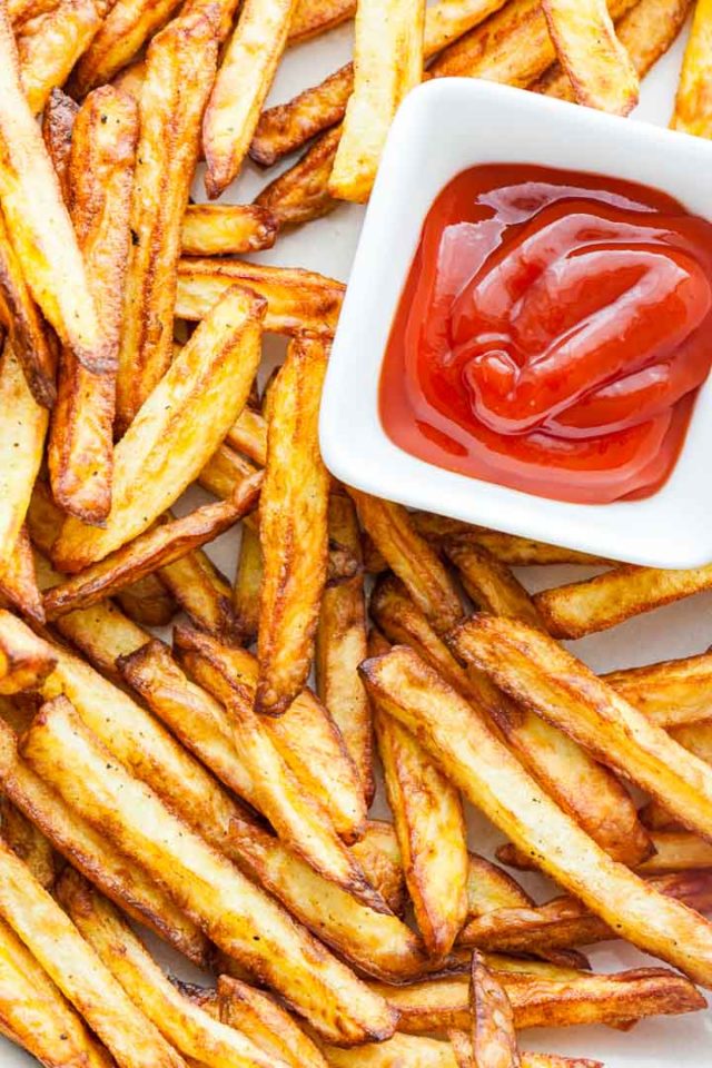 Top-down shot of brown, crispy fries with a small, white, rectangular bowl of ketchup.