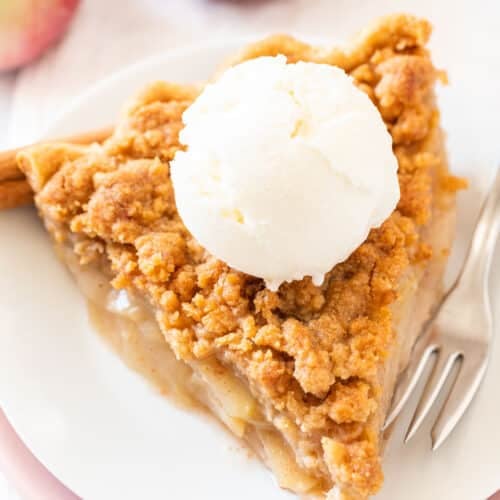 A slice of apple crumble pie on a white plate topped with vanilla ice cream.