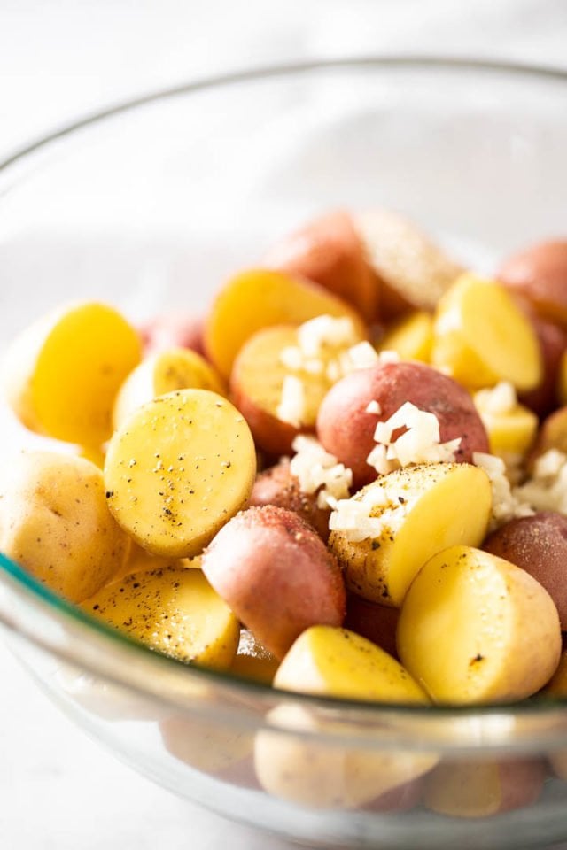 raw, halved young potatoes in a glass bowl, seasoned with oil, salt, pepper and minced garlic.