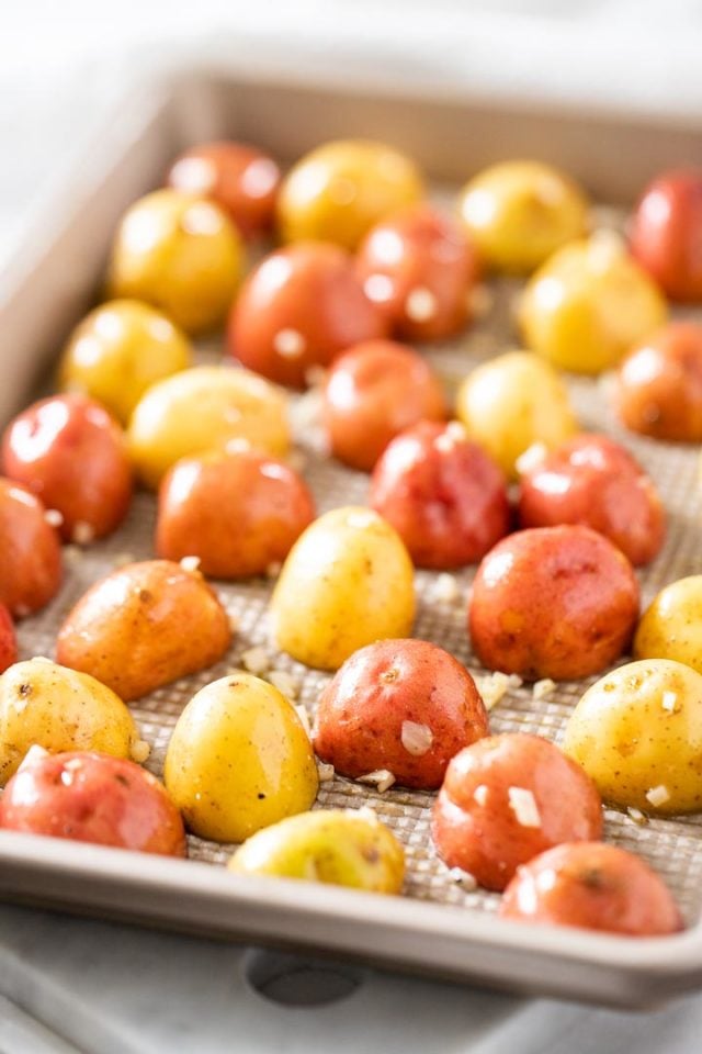 raw, halved young potatoes with garlic lying cut side down in a baking sheet.
