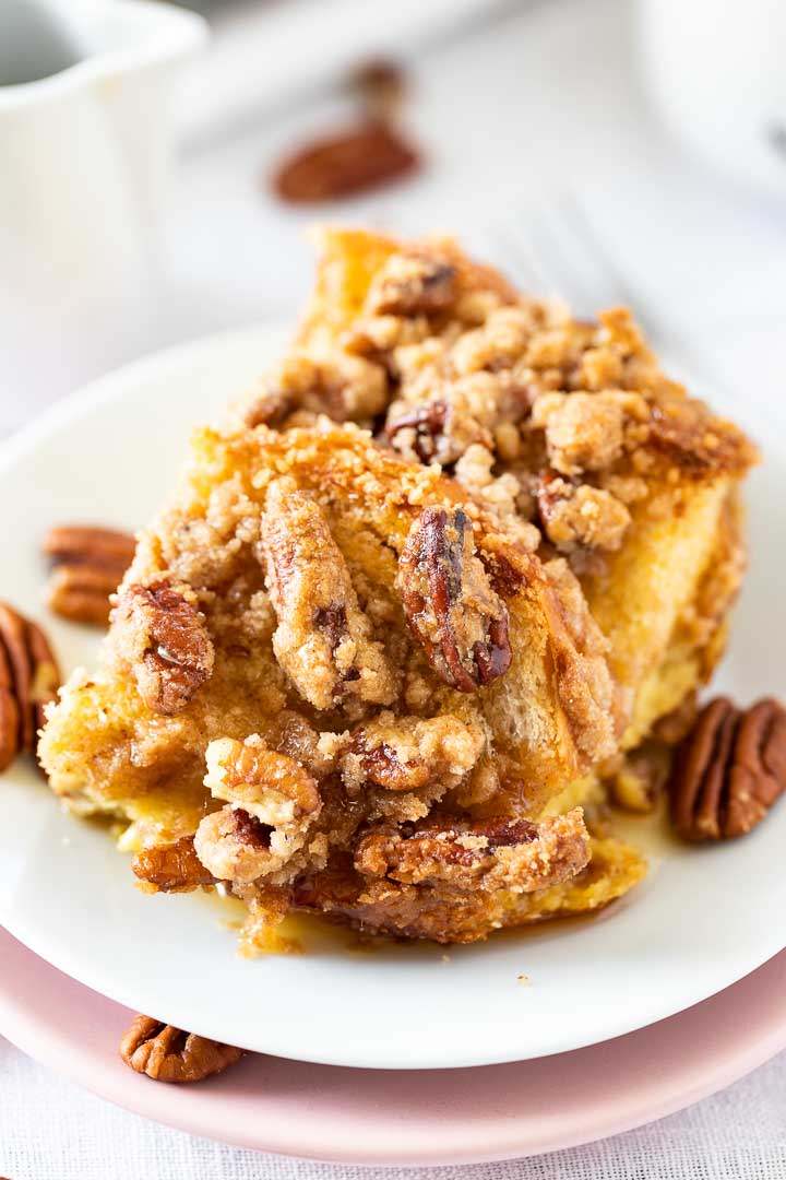 Close-up of a piece of french toast casserole on a white plate garnished with pecans.