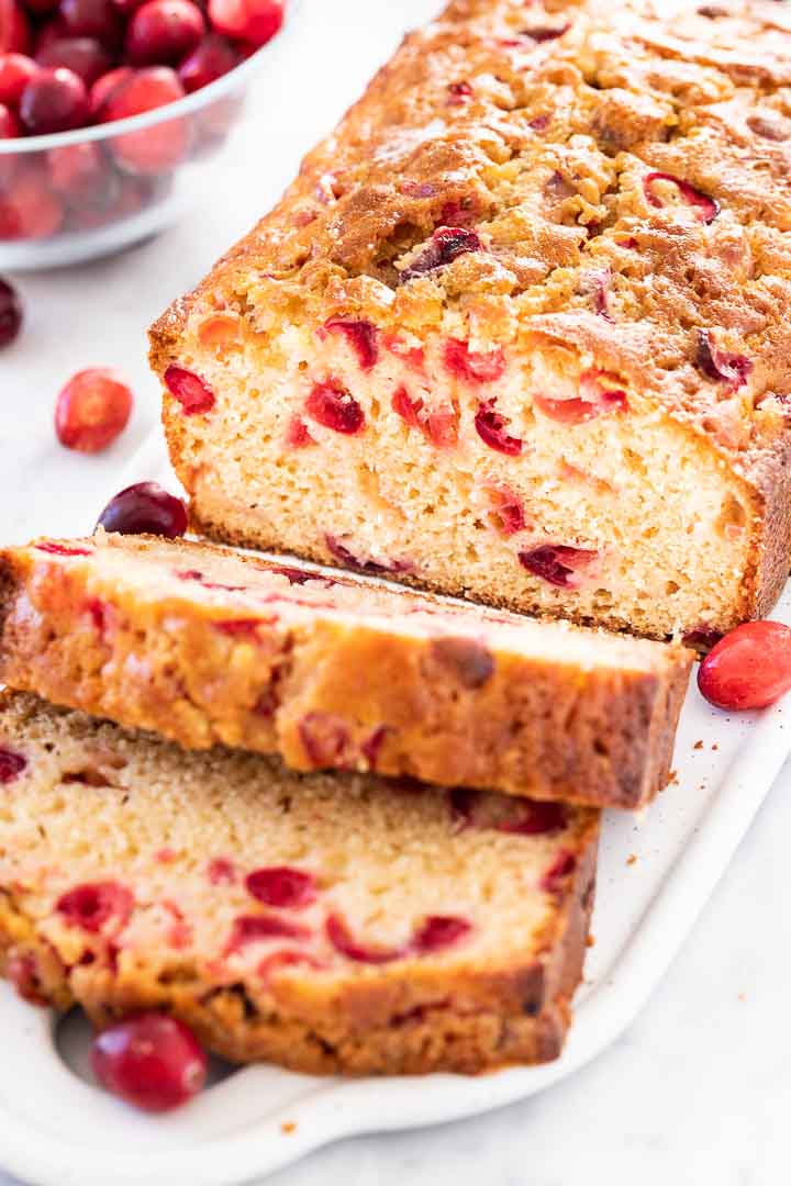 Close-up of Cranberry Orange Bread on a grey rectangular serving platter garnished with cranberries. Two slices have been cut off and are fallen over.