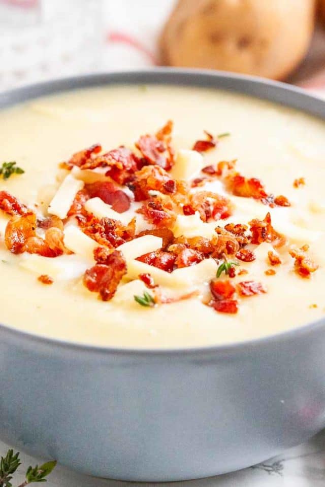 Close-up of a grey bowl of potato soup topped with bacon crumbs, cheese stripes and thyme.